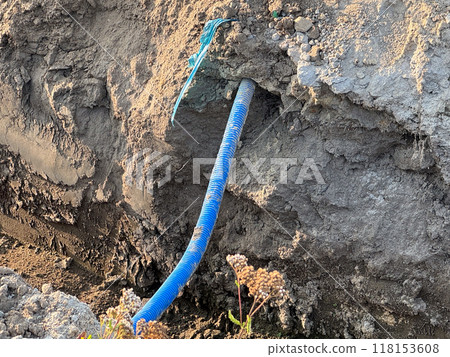 A blue corrugated pipe partially exposed in a dirt trench at a construction site 118153608