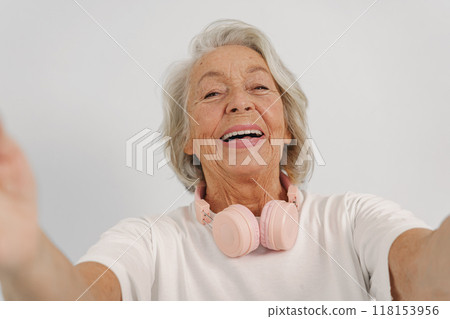 A Joyful Elderly Woman is Enjoying Life to the Fullest while Wearing Headphones and Smiling 118153956