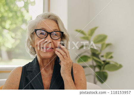 A Cheerful Senior Woman Smiling While Engaged in a Phone Conversation in a Bright Interior Space 118153957