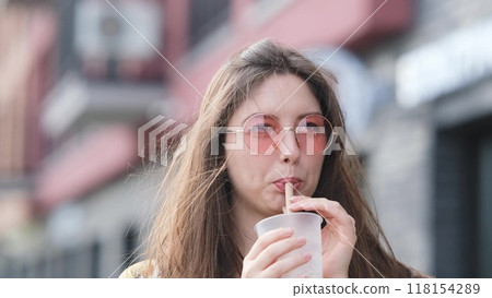 Pensive happy woman sipping a milkshake in the street Pensive happy woman sipping a milkshake in the street 118154289