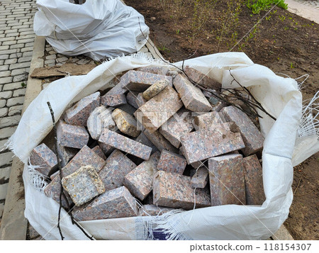 There is a white garbage bag with fragments of bricks on the sidewalk. There is a white garbage bag with fragments of bricks on the sidewalk. 118154307