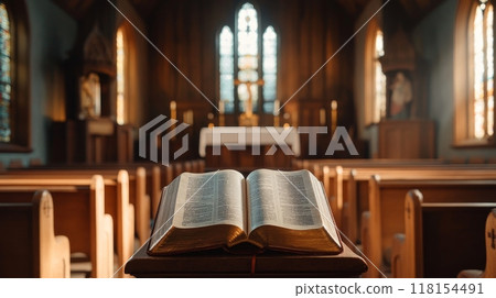 Open Bible on wooden stand in foreground of empty church interior, with altar, stained glass windows, and pews visible, symbolizing faith and worship 118154491