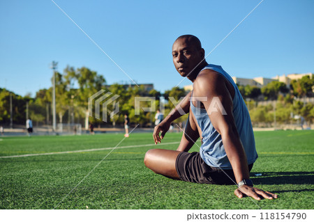 Athletic man sitting on grassy sports football field look at camera Athletic man sitting on grassy sports football field look at camera 118154790