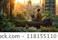 A person working on a laptop on a rooftop garden with a cityscape view at sunset 118155110