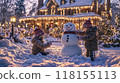 Children building a snowman together in front of a house decorated with Christmas lights 118155113