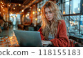 A young woman working on her laptop in a cozy cafe, surrounded by warm lighting 118155183