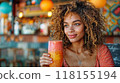 A woman enjoying a fresh smoothie in a cozy cafe, smiling with natural light streaming in 118155194