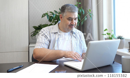 A man works on a computer. He looks at the screen and types on the keyboard. Perfect for content about remote work, freelancing and office work. 118155382