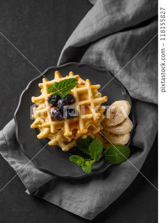 A stack of belgian waffles with kiwi, banana slices and mint, drizzled with honey syrup A stack of belgian waffles with kiwi, banana slices and mint, drizzled with honey syrup 118155827