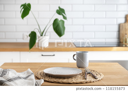 Wooden table top with plate and cup for breakfast against blurred white kitchen with cutting board 118155873