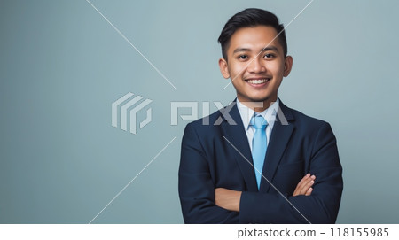Confident Young Indonesian Businessman in Professional Suit Smiling with Arms Crossed Against Light Background 118155985