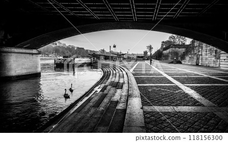 Ducks glide along the calm waters beneath the Jena Bridge, while a quiet walkway stretches alongside the Seine River in Paris, creating a peaceful urban atmosphere during the day. Ducks glide along the calm waters beneath the Jena Bridge, while a quiet walkway stretches alongside the Seine River in Paris, creating a peaceful urban atmosphere during the day. 118156300