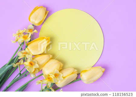 Spring flower of yellow tulips and daffodils on purple background with around yellow round shape made of paper for text. Flat lay, copy space. Hello spring Spring flower of yellow tulips and daffodils on purple background with around yellow round shape made of paper for text. Flat lay, copy space. Hello spring 118156523