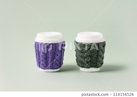 Two cups made of cardboard for takeaway coffee with knitted green and purple cover and white bioplastic lid. Concept of takeaway coffee, walking, energetic life Two cups made of cardboard for takeaway coffee with knitted green and purple cover and white bioplastic lid. Concept of takeaway coffee, walking, energetic life 118156526