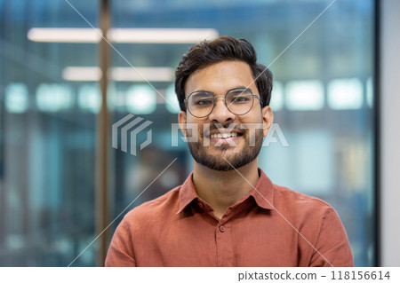 Confident businessman wearing casual shirt smiling in modern office. Positive expression signifies readiness for productive workday. Represents success, leadership, and corporate environment. 118156614