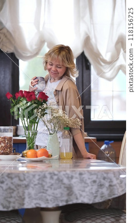 Cute blonde in the kitchen, drinking morning coffee. She holds a mug with a hot drink in her hands. A woman living alone enjoys a peaceful day off. Cute blonde in the kitchen, drinking morning coffee. She holds a mug with a hot drink in her hands. A woman living alone enjoys a peaceful day off. 118156725