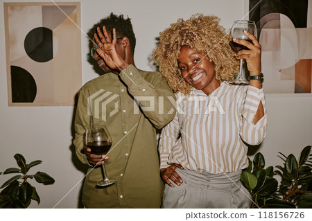 Portrait of young beautiful woman smiling to camera and her colleague hiding face while partying in office 118156726