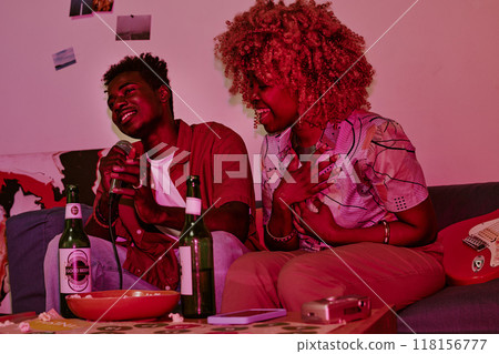 Young people sitting on sofa and singing loudly together while they illuminated with neon pink light Young people sitting on sofa and singing loudly together while they illuminated with neon pink light 118156777