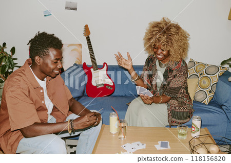 Happy friends sitting at wooden table and playing cards in cozy living room Happy friends sitting at wooden table and playing cards in cozy living room 118156820