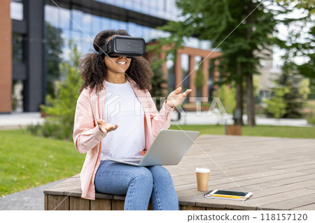 Woman using VR headset and laptop outside, symbolizing innovation and technology in a modern city environment. 118157120