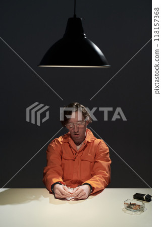 Illuminated Man in Orange Attire Sitting Under Hanging Lamp Illuminated Man in Orange Attire Sitting Under Hanging Lamp 118157368