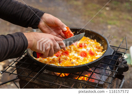 A man slices tomatoes in order to fry them with eggs A man slices tomatoes in order to fry them with eggs 118157572
