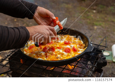 A man slices tomatoes in order to fry them with eggs 118157574