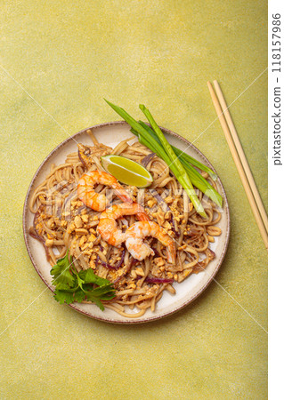 Bowl of pad thai noodles garnished with shrimps and lime on green background, traditional dish of Thailand Bowl of pad thai noodles garnished with shrimps and lime on green background, traditional dish of Thailand 118157986