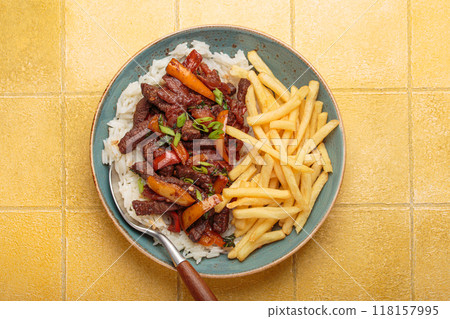 Lomo saltado with french fries and rice on yellow tiles background, traditional Peruvian dish Lomo saltado with french fries and rice on yellow tiles background, traditional Peruvian dish 118157995