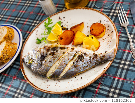 Baked in oven dorado fish with lemon and potatoes served on plate closeup 118162362