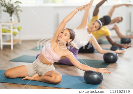 Young woman performing side bend with exercise ball during Pilates class 118162529