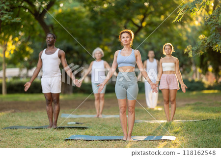 Woman performing Mountain Pose during group yoga class in park 118162548