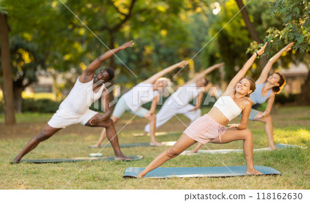Girl doing Utthita Parsvakonasana during group yoga workout in park 118162630