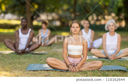 Multinational yoga enthusiasts with female coach perform Baddha konasana in park 118162644