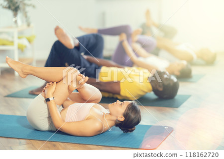 Young woman coach and students perform Supta kapotasana during training in studio 118162720