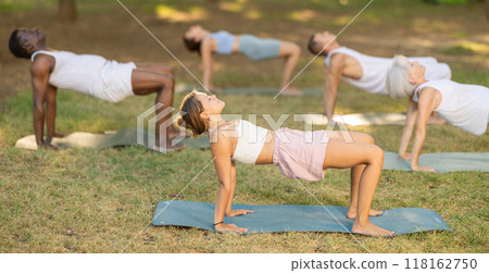 Girl performing Reverse Table Pose during group yoga in park 118162750