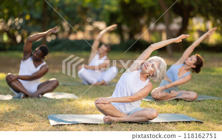 Elderly woman stretching in lotus position during group yoga in park Elderly woman stretching in lotus position during group yoga in park 118162751