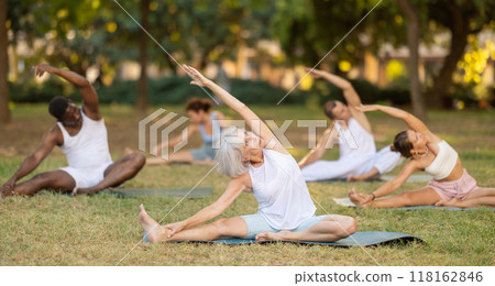 Multinational yoga enthusiasts with female coach perform Janu Shirshasana in park Multinational yoga enthusiasts with female coach perform Janu Shirshasana in park 118162846