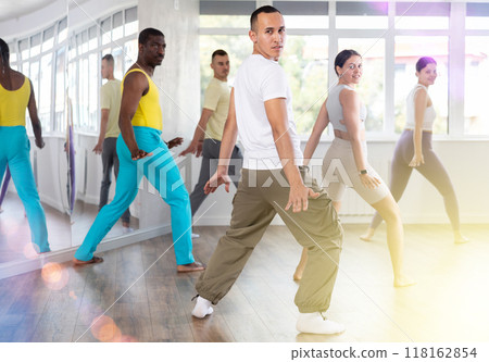 Happy multinational young man and woman dancing and training latin dance movements in ballroom together 118162854