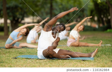 Multinational yoga enthusiasts with African male coach perform Janu Shirshasana in park Multinational yoga enthusiasts with African male coach perform Janu Shirshasana in park 118162864