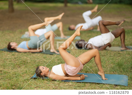 Girl doing One Legged Bridge Pose during group yoga in park 118162870