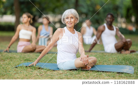 Multinational yoga enthusiasts with senior female coach perform padmasana in park Multinational yoga enthusiasts with senior female coach perform padmasana in park 118162888