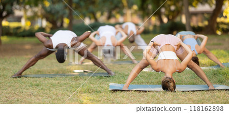 Girl performing Prasarita Padottanasana with group during yoga class in park Girl performing Prasarita Padottanasana with group during yoga class in park 118162898