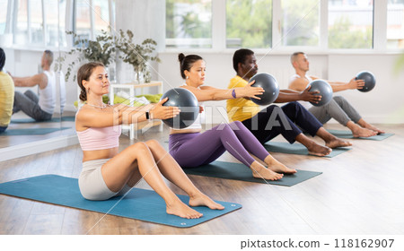 Sporty girl doing sit-ups with medicine ball during group pilates class 118162907