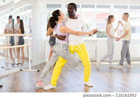 Happy African american man in pair with young woman dancing and training latin dance movements in ballroom together Happy African american man in pair with young woman dancing and training latin dance movements in ballroom together 118162952