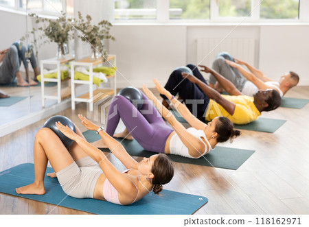Men and girls hold fitball in their lap, raise and lower torso Men and girls hold fitball in their lap, raise and lower torso 118162971