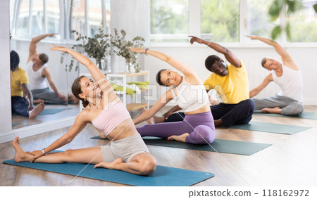 Young woman coach and students perform Janu Shirshasana during training in studio 118162972