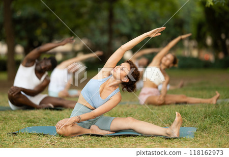 Multinational yoga enthusiasts with female coach perform Janu Shirshasana in park 118162973