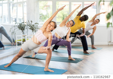 Young woman coach and students perform Parighasana during training in studio Young woman coach and students perform Parighasana during training in studio 118162987