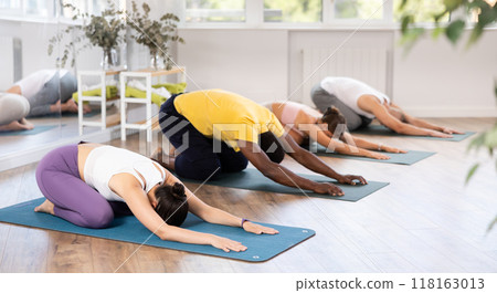Young woman coach and students perform balasana during training in studio 118163013